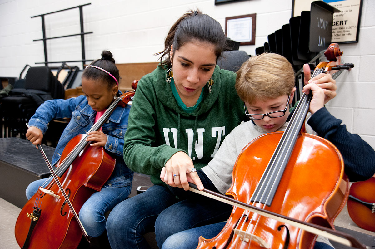 A teacher helping an elementary student play cello.